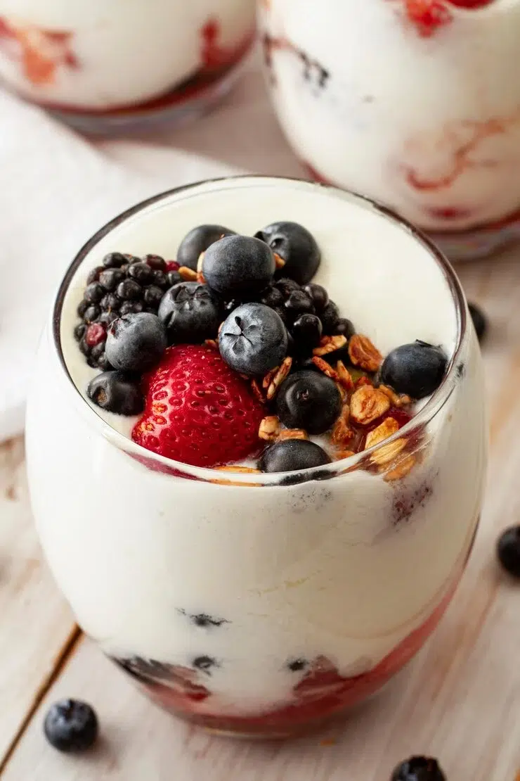 Quarkcreme mit frischen Beeren wie Erdbeeren, Heidelbeeren und Brombeeren, serviert im Glas mit knusprigem Granola.